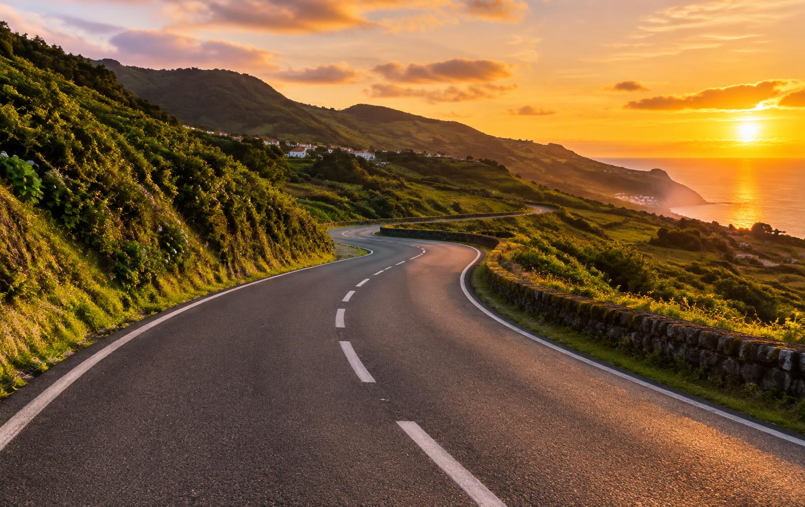 Estrada sinuosa com linhas brancas ao pôr do sol